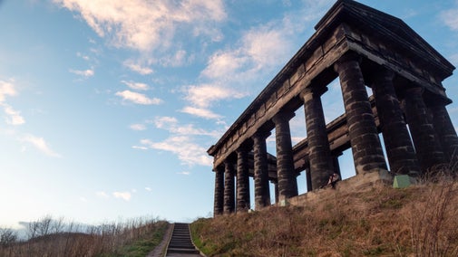 View of a large grey columned building at dusk with some wooden steps going up to it.